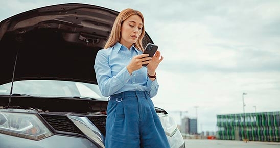 Femme consultant son téléphone contre sa voiture