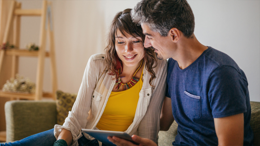 Une femme et un homme assis sur un canapé regardant une tablette