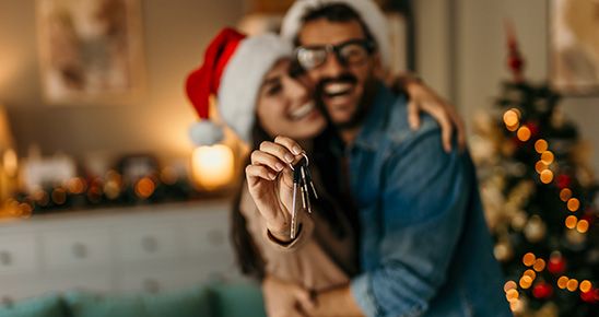 Couple homme femme , en tenue de Noël, présentant la clef de leur logement