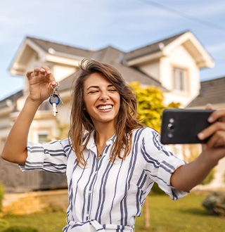 Dame qui prend un selfie devant une maison, ses clés en main 