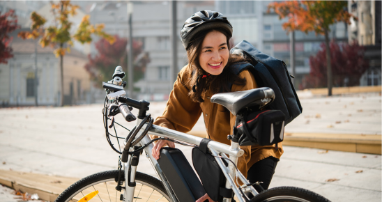 Femme souriante derrière son vélo électrique en extérieur par beau temps